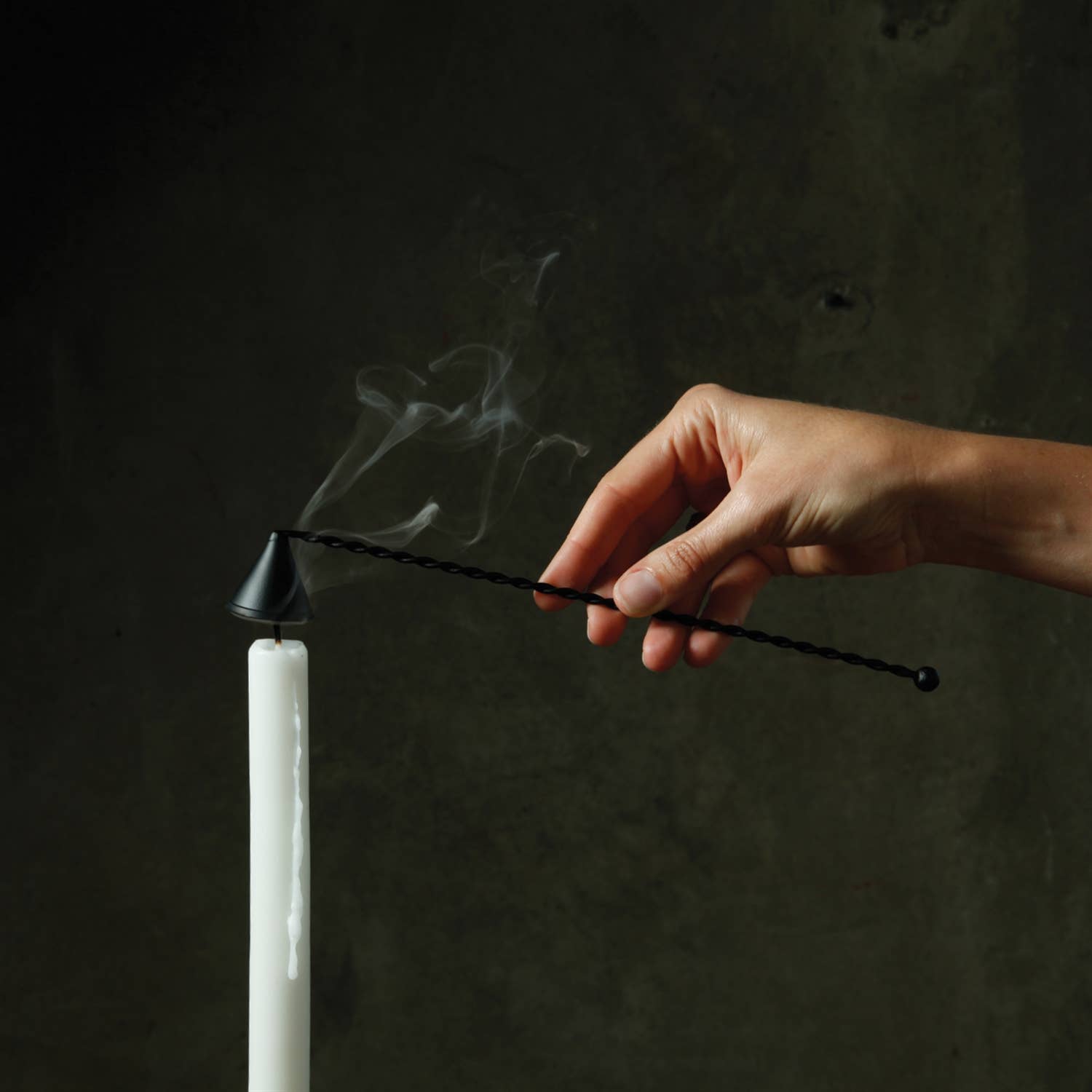 Hand lighting a white candle with a black wick against a dark background