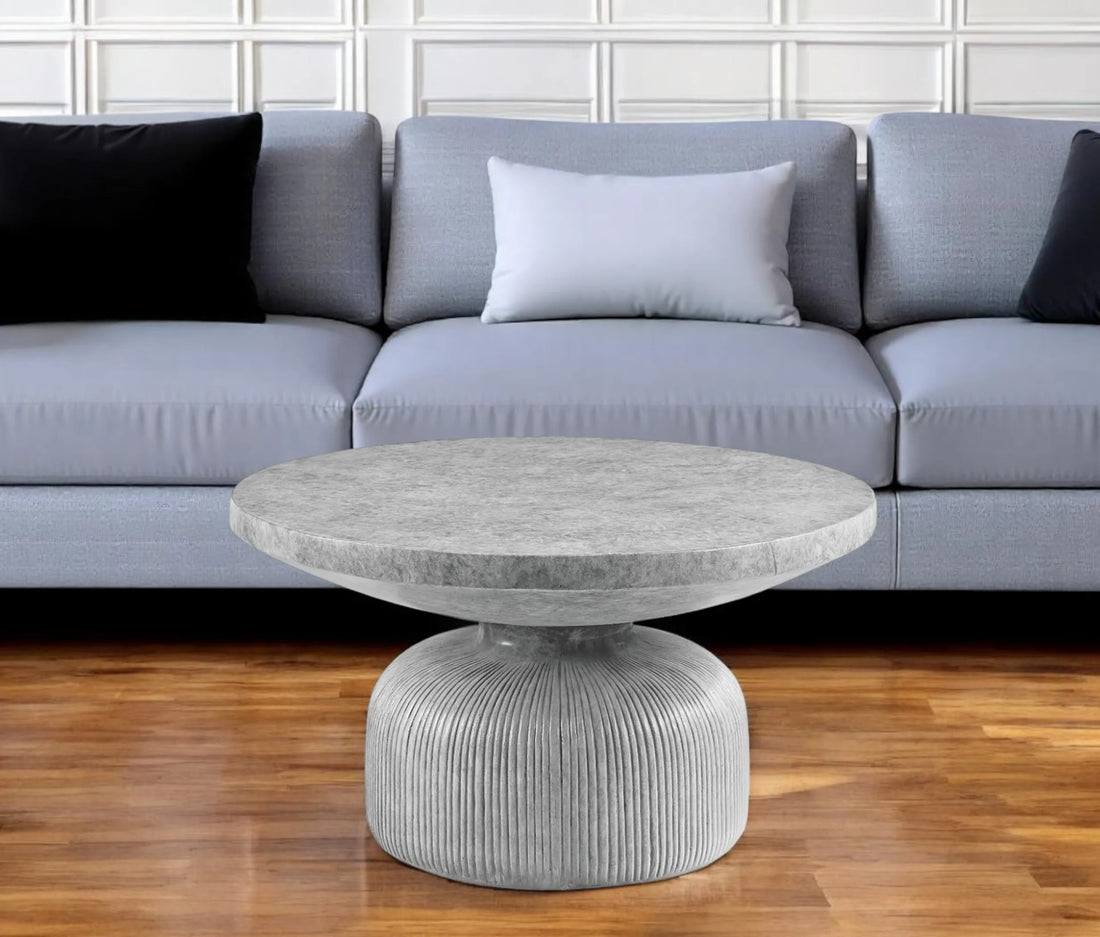 Round stone coffee table in front of a gray sofa with black and white cushions.