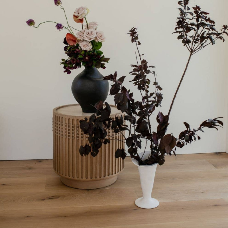 Vases with flowers on a wooden surface against a white wall