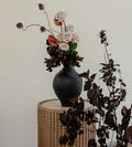Black vase with flowers on a wooden table against a plain background