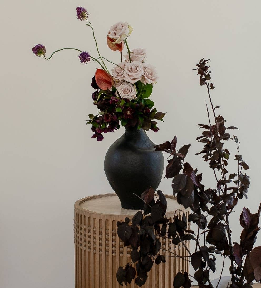 Black vase with flowers on a wooden table against a plain background