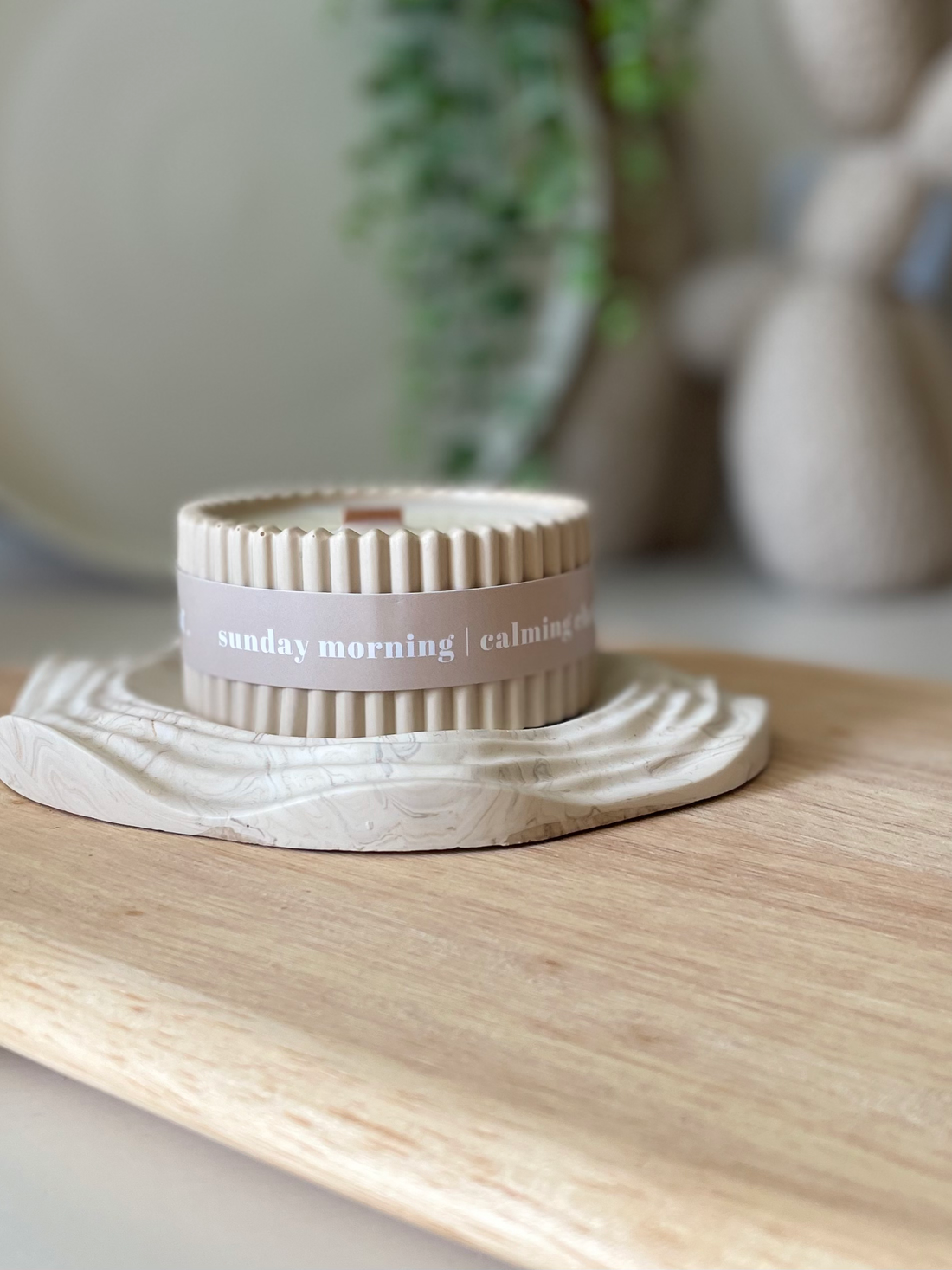Candle with a label on a wooden surface, surrounded by neutral decor