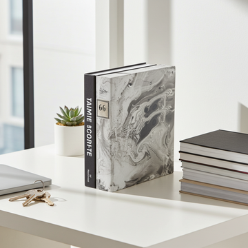 Book with a marble design on a desk next to a plant and keys