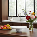 Modern kitchen with a fruit plate, white cake stand, and vase of flowers on a wooden counter.