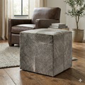 Gray textured ottoman in a living room setting with a brown armchair and books.