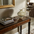 Console table with decorative items including a vase, books, and a magnifying glass in a living room setting.