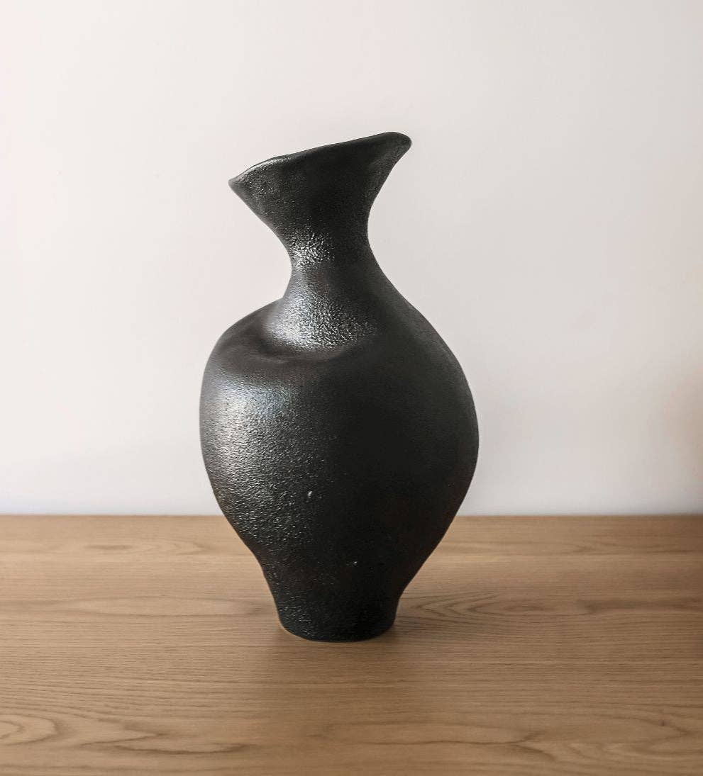 Black ceramic vase on a wooden surface with a white background