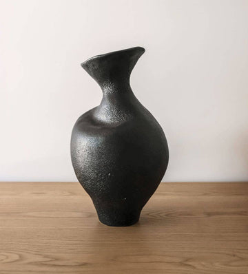 Black ceramic vase on a wooden surface with a white background