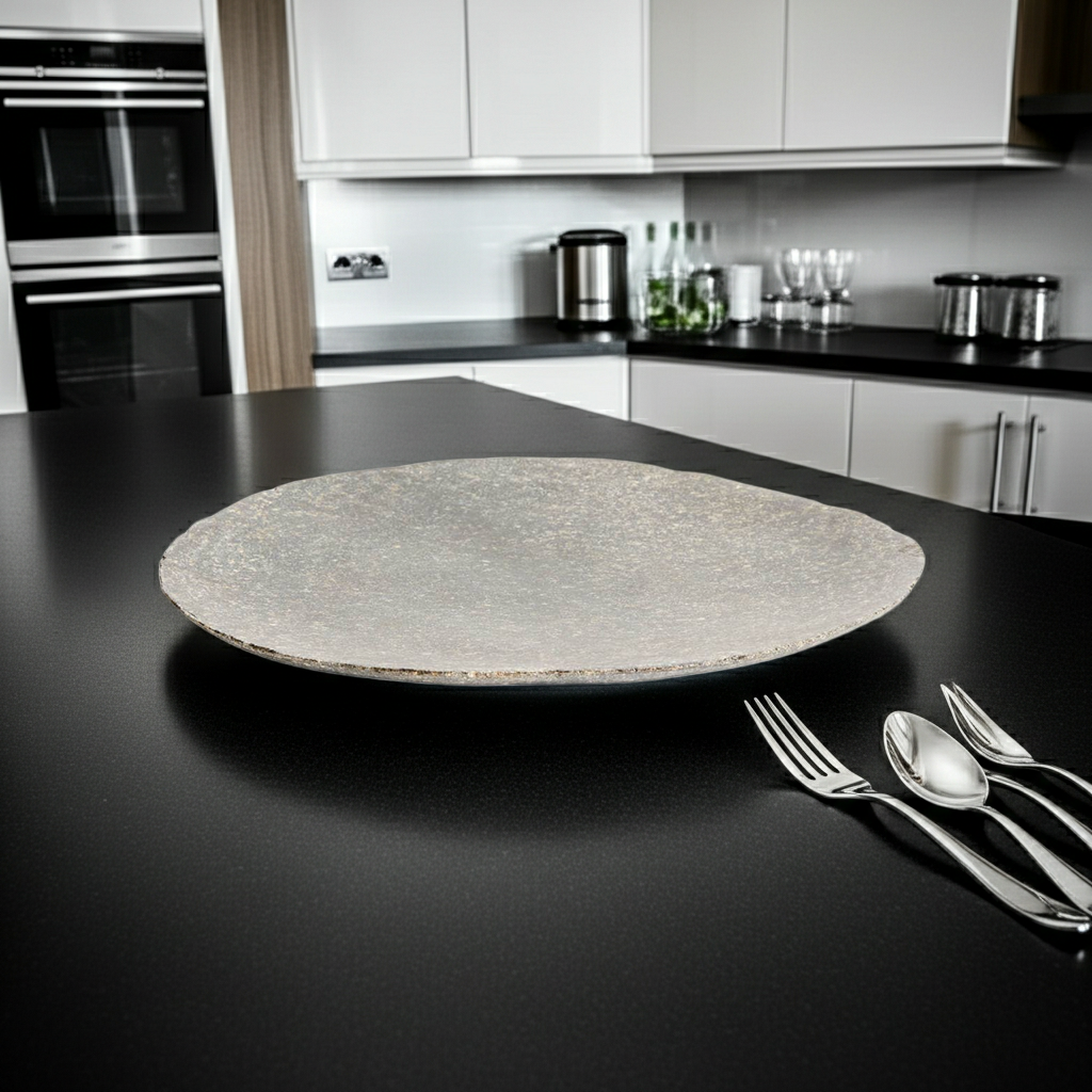 Round stone cutting board on a black kitchen counter with silverware.