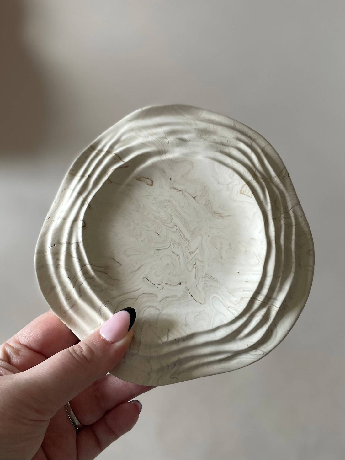 Hand holding a ceramic dish with textured surface against a neutral background