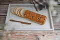 Loaf of bread with slices on a marble tray with a knife, on a wooden surface.