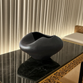 Black ceramic vase on a marble surface with a textured wall in the background